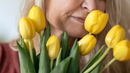 Blond senior woman with eyes closed smelling fresh yellow tulip flowers at home